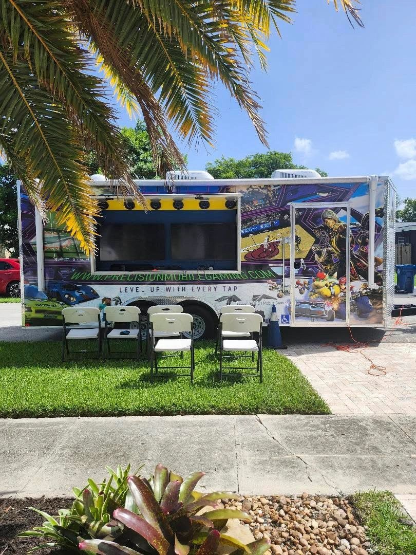 Precision Mobile Gaming trailer parked on a residential street with exterior screen open and chairs set up on the lawn